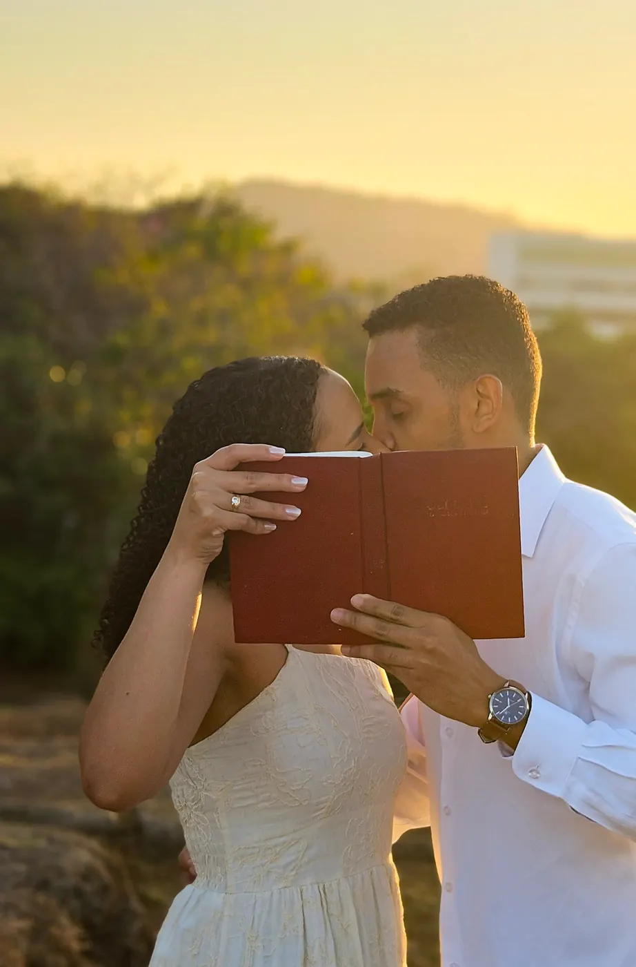 Andressa e Káhio se beijando atrás de uma Bíblia ao pôr do sol